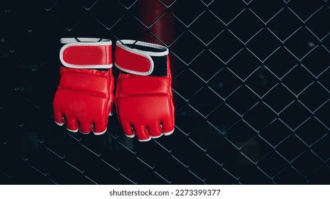 Red Gloves for MMA Boxers fighter hang on ring octagon black wall. Concept sport banner.