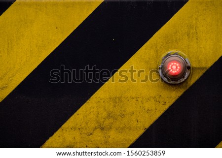 Red glowing status indicator, warning button or lamp on yellow & black panel.