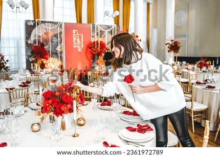 Red gold color flower decor for Chinese New Year celebration. Girl woman florist, decorator, organizer of events, parties, wedding planner making floral arrangement, festive bouquet, table decoration.