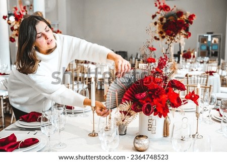 Red gold color flower decor for Chinese New Year celebration. Girl woman florist, decorator, organizer of events, parties, wedding planner making floral arrangement, festive bouquet, table decoration.