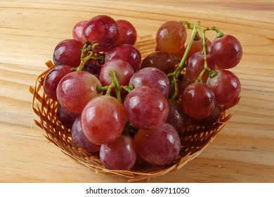 Red grape on the basket over wooded background.