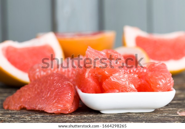 red grapefruit divided into pieces on\
a black table, close-up of citrus juicy and\
delicious