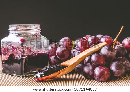 Red grapes and jam on wooden table with black background