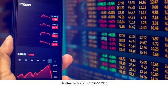 Red Graph On Smartphone With Blurry Computer Monitor Showing Stock Price Slump. The Concepts Of The Economic Downturn From Covid 19 And World Fuel Energy.