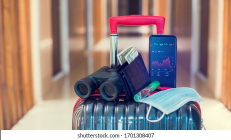 Red Graph On Smartphone With Medicine Mask, Wallet, Dollar Bill, Binoculars And Travel Equipment On Luggage In Hotel. The Concepts Of The Economic Down Turn From Covid 19. Travel Business Downturn.