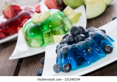 Red, green and blue Jello with fresh fruits on wooden background
