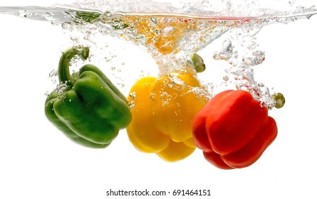 red, green, yellow bell pepper falls to the water, causing bubbles and scattered water.