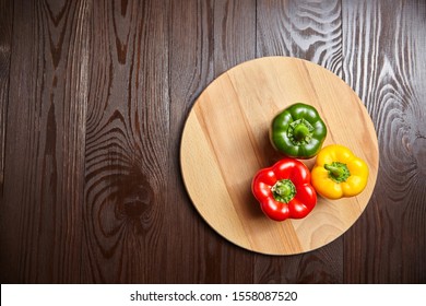 Red, green, and yellow bell peppers, cutting board on wooden background with copy space. Three sweet peppers in different colors on brown table, vegetable ingredient, healthy food, top view - Shutterstock ID 1558087520