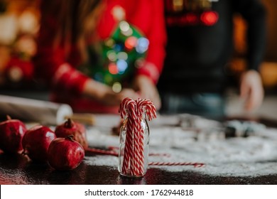 Red Grenades, Christmas Sweets And Flour Laying On A Table Against A Couple In Red And Black Christmas Sweaters. Low Key.