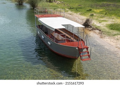 Red And Grey Pleasure Craft Sailing Boat Moored By The Side Of A Clear Green River