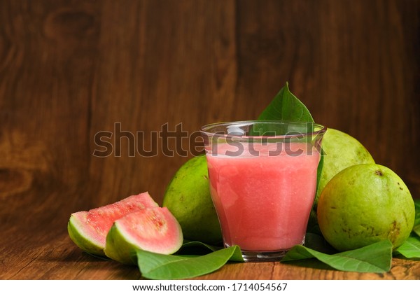 red guava juice is served on\
a wooden background with guava fruit slices and leaf\
decorations