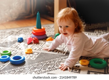 Red Hair Baby On The Floor. Child Laying On The Carpet At Home And Playing With Toys. Portrait Of The Cute Infant Girl. Colorful Toys And A Pyramid On The Floor. 