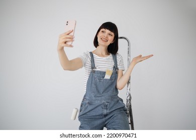 Red hair girl with cute smile holds a paint roller and smart phone in her hands. Young woman leaning on a ladder that she uses during repairs and having video call on her phone. - Powered by Shutterstock