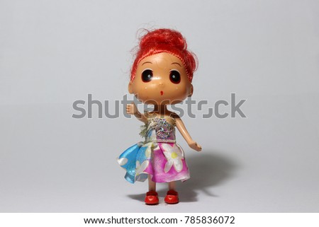 Red hair girl doll in colorful dress on the white floor. doll is a small model of a human figure, often one of a baby or girl, used as a child's toy.