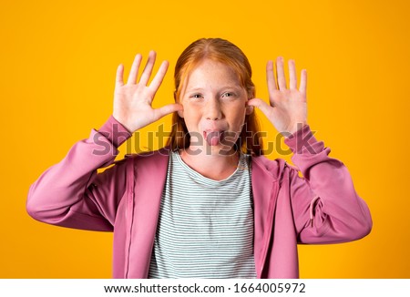 Red hair girl taunting and mocking while sticking her tongue out. Young Caucasian pre teen girl being rude and making funny faces with her tongue and hands.