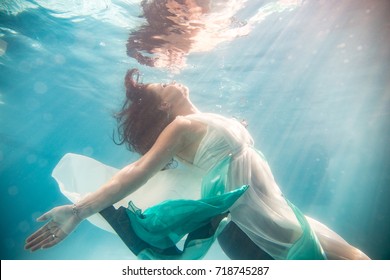 A Red Hair Woman In A White And Blue Dress, Floating Underneath The Water