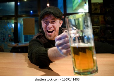 Red haired almost Irish guy seating in the bar and drinks some beer and looks at you and cheers with funny face
