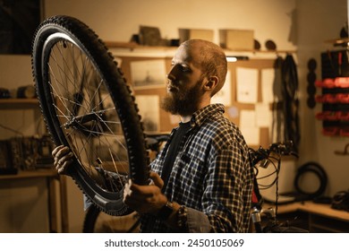 Red Haired bearded male worker holding and repairing bicycle wheel while standing in bicycle workshop. Copy space - Powered by Shutterstock