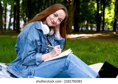 Red Haired Caucasian Woman Studying Remotely On Laptop, Writing Down Information In Notebook, Outside.Education Concept. Homework