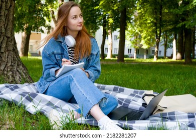 Red Haired Caucasian Woman Studying Remotely On Laptop, Writing Down Information In Notebook, Outside