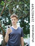 Red haired european guy with freckles on his face and arms and body in the garden posing and looking at and playing with his huawei mobile phone