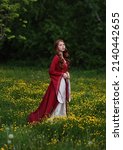 Red haired maiden in medieval dress walking in field of yellow flowers. Fantasy historical portrait