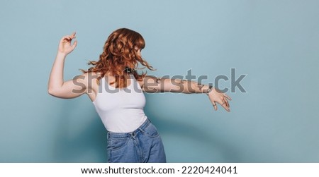 Red haired woman dancing while standing in a studio. Woman having fun in casual clothing.