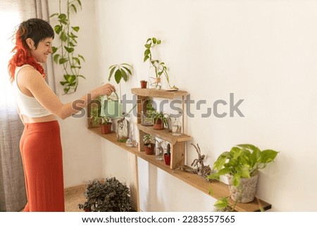 red haired woman at home watering plants, woman surrounded by plants, white wall, smiling