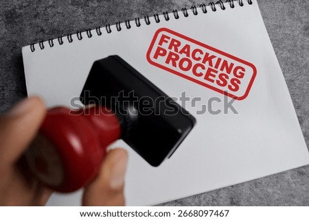 Red Handle Rubber Stamper and Fracking process text above book isolated on wooden background