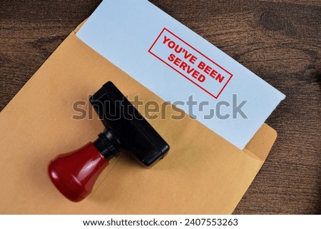 Red Handle Rubber Stamper and You've Been Served text above brown envelope isolated on wooden background