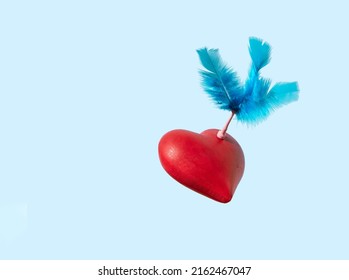 Red Hart And Bright Blue Fluffy Feathers, Creative Arrangement Against Pastel Background. Love Concept, Cupid Arrow Idea.