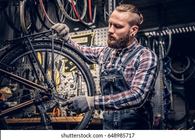 Red head bearded mechanic fixing rear derailleur from a bicycle in a workshop. - Powered by Shutterstock