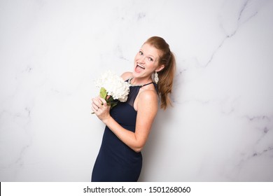 Red Head Bridesmaid With White Flowers Against White Marble Backdrop For Photobooth