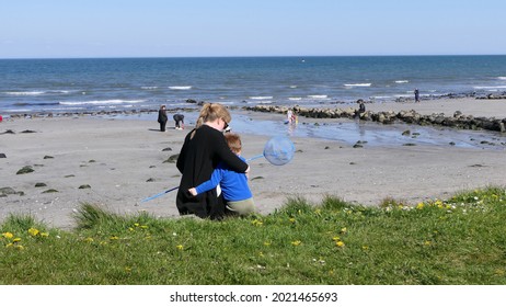 Red Headed Boy And Mother Playing With A Fishing Net On A Sandy Beach In Ireland