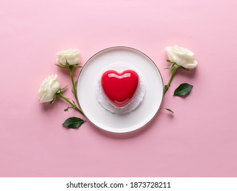 red heart cake on white plate and delicate white roses. Concept Valentines Day, Mothers Day, Womens Day. pink background. copy space