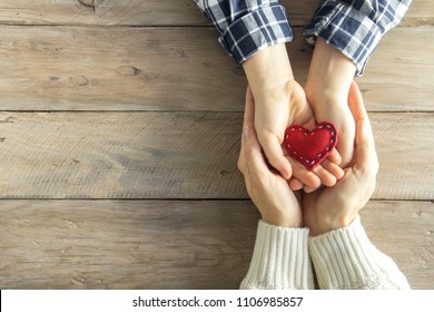 Red Heart In Child And Female Hands Over Wooden Background, Copy Space. Kindness, Family, Love And Charity Concept, Hand Made Valentine Or Mother's Day Gift.