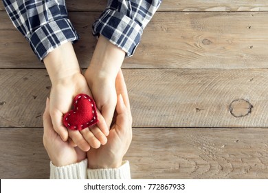 Red Heart In Child And Female Hands Over Wooden Background, Copy Space. Kindness, Family, Love And Charity Concept, Hand Made Valentine Or Mother's Day Gift.