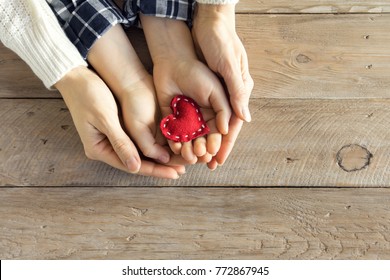 Red Heart In Child And Female Hands Over Wooden Background, Copy Space. Kindness, Family, Love And Charity Concept, Hand Made Valentine Or Mother's Day Gift.