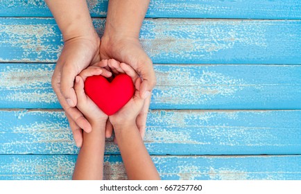 Red heart in child kid and mother hands on old blue wooden table in vintage retro style