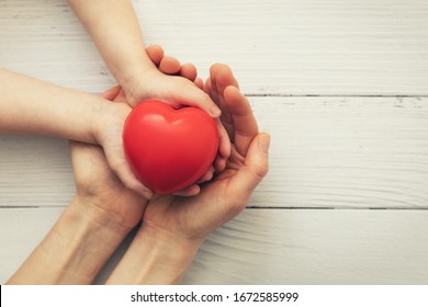 red heart in child and mother hands on white wooden background. concept of love, charity, empathy
