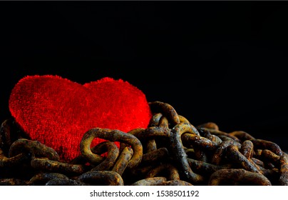 The Red Heart Was Covered With Rusty Chains Over Black Background Copy Space For Text. The Concept Of The Heartbreaking Anguish, Distress Hurt And Anguish Valentine. Content Of Arranged Marriage.