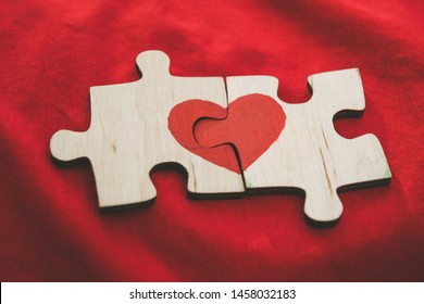 Red heart is drawn on the pieces of the wooden puzzle lying next to each other on red background. Love concept. St. Valentine day