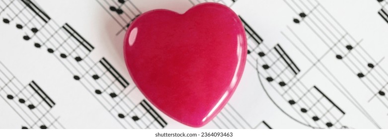Red heart on paper with musical notes close up. Concept of romantic music and love songs.