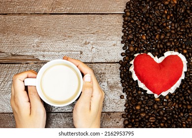 red heart on  Roasted coffee beans and hands woman drink holding cup of milk coffee on wood table, love coffee concept