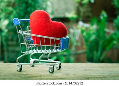 Red Heart On Small Shopping Cart On Wooden Table With Nature Background. Healthcare And Medical Or Buy Health Insurance Concept.