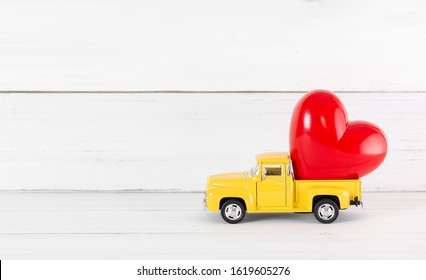 Red Heart on Toy Yellow Pickup Car on white wood background. Travel Love Concept with Copy Space.