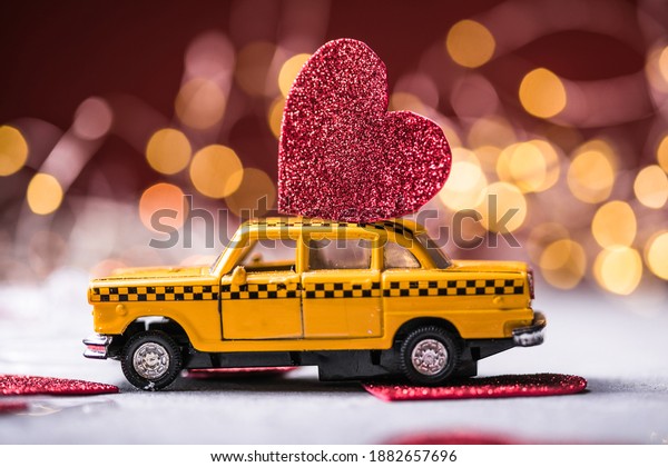Red heart on toy yellow  taxi\
car on red background. Travel love concept with copy\
space.