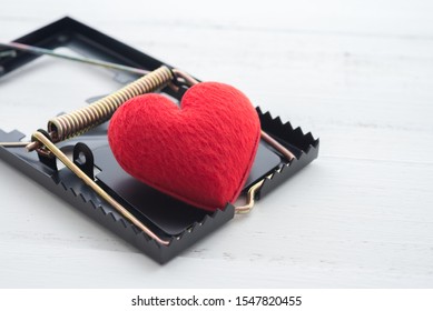 Red heart in a rat trap on white wooden background. Online internet romance scam or valentine day in darkside concept. Love is bait or victim.