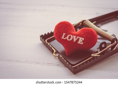 Red Heart In A Rat Trap On White Wooden Background. Online Internet Romance Scam, Swindler Or Valentine Day In Darkside Concept. Love Is Bait Or Victim.