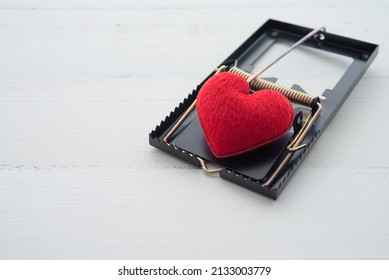 Red heart in a rat trap on white wooden background. Online internet romance scam, swindler or valentine day in darkside concept. Love is bait or victim.